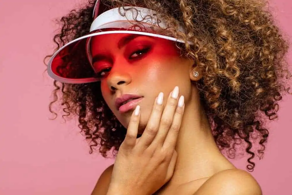 black girl with curly hair wearing a red sun visor touching her face