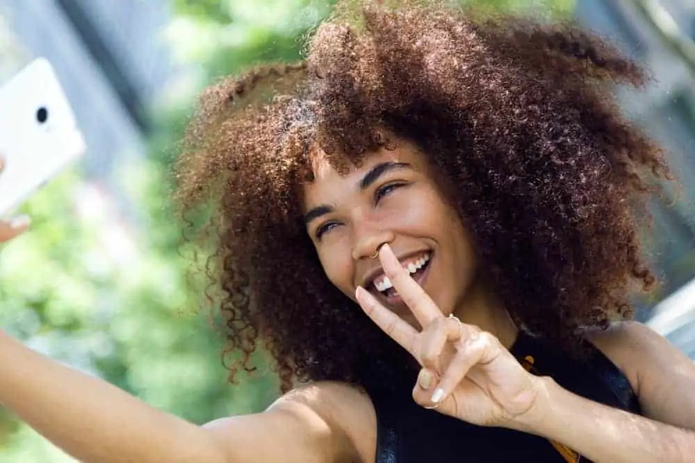 A cute African American female takes a selfie while showing off her bouncy curls styled with grapeseed oils.