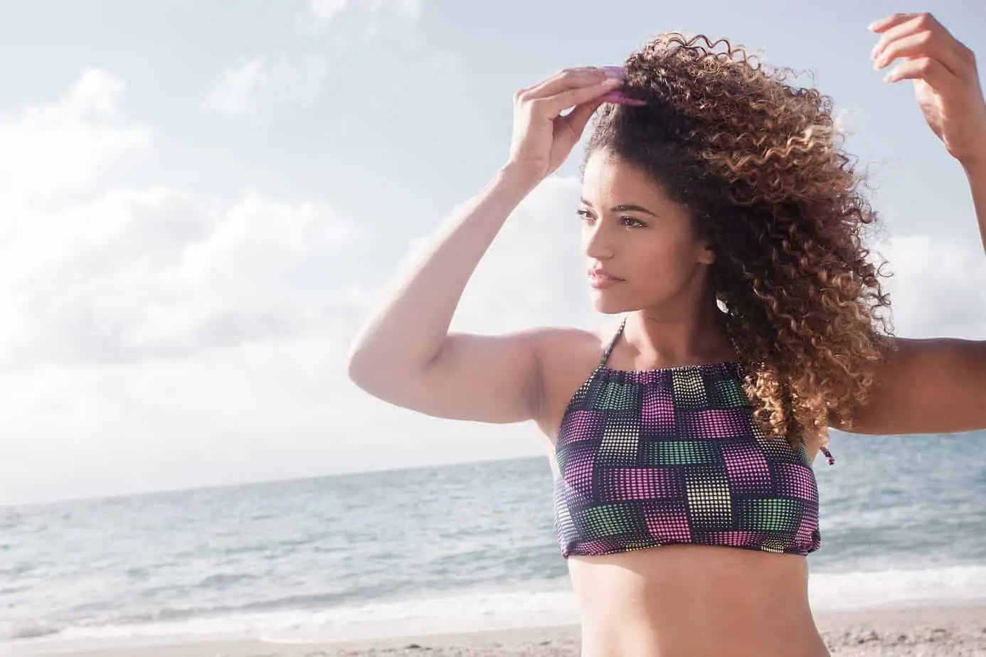 Gorgeous female combing her type 3a curly hair on the beach with an afro pick.