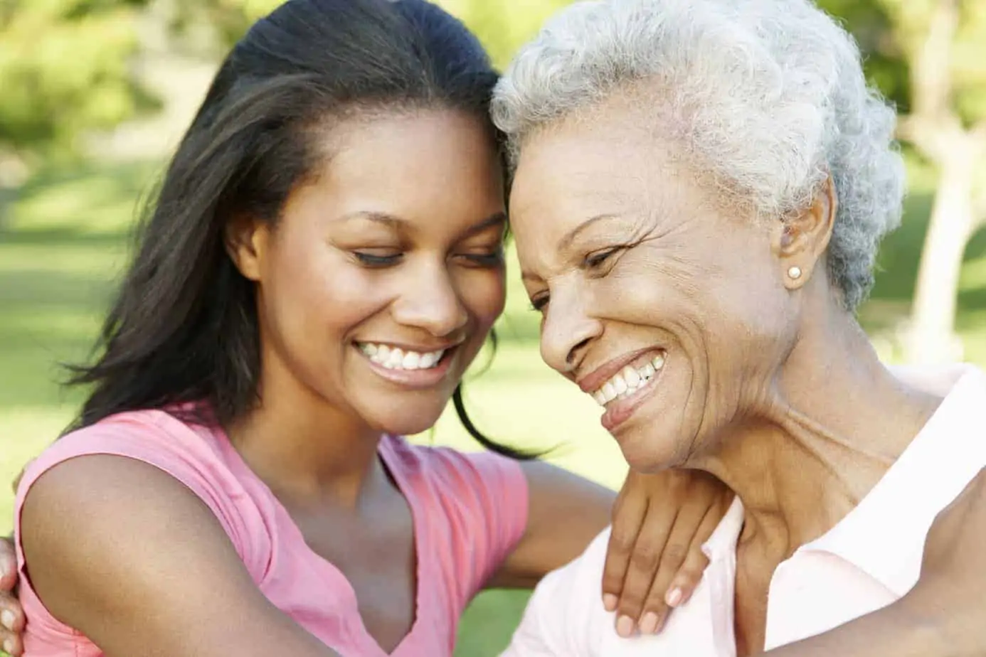 Mother and daughter sitting on a park bench smiling.