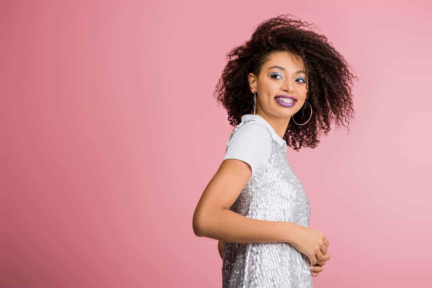 female with curly hair wearing make-up looking back at the camera