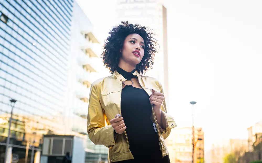 Beautiful African American young woman wearing a gold jacket and black dress with curly hair.