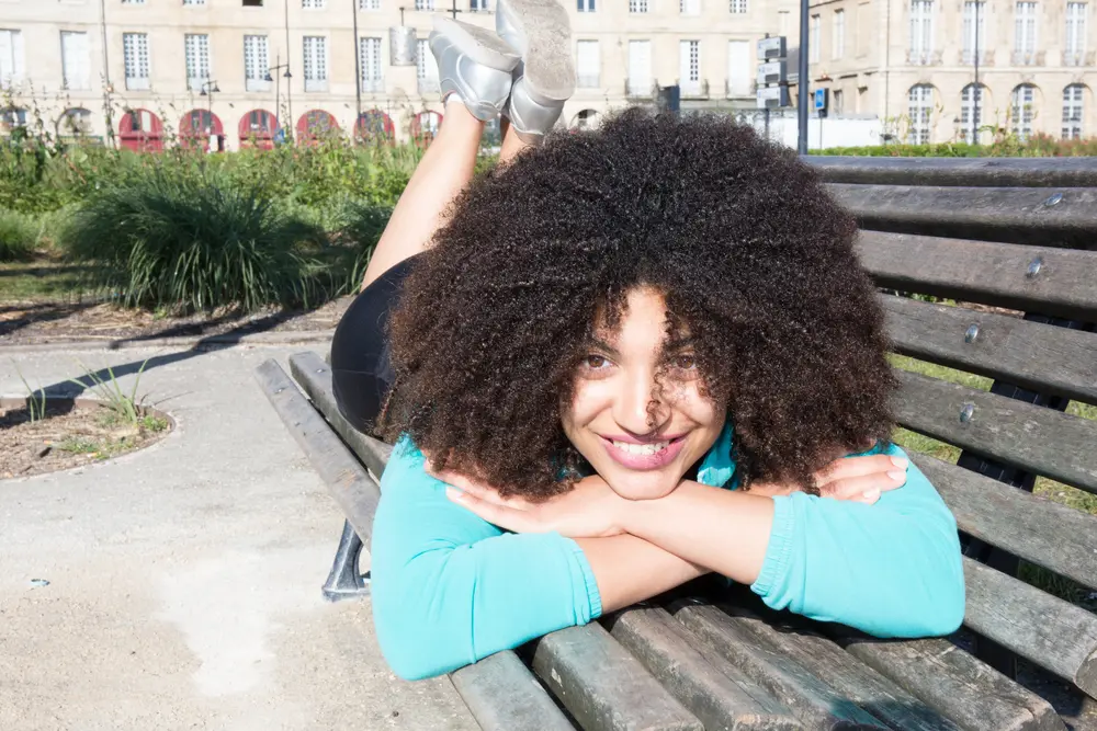 Young beautiful mixed race American woman lying on a bench in the city with naturally curly hair.