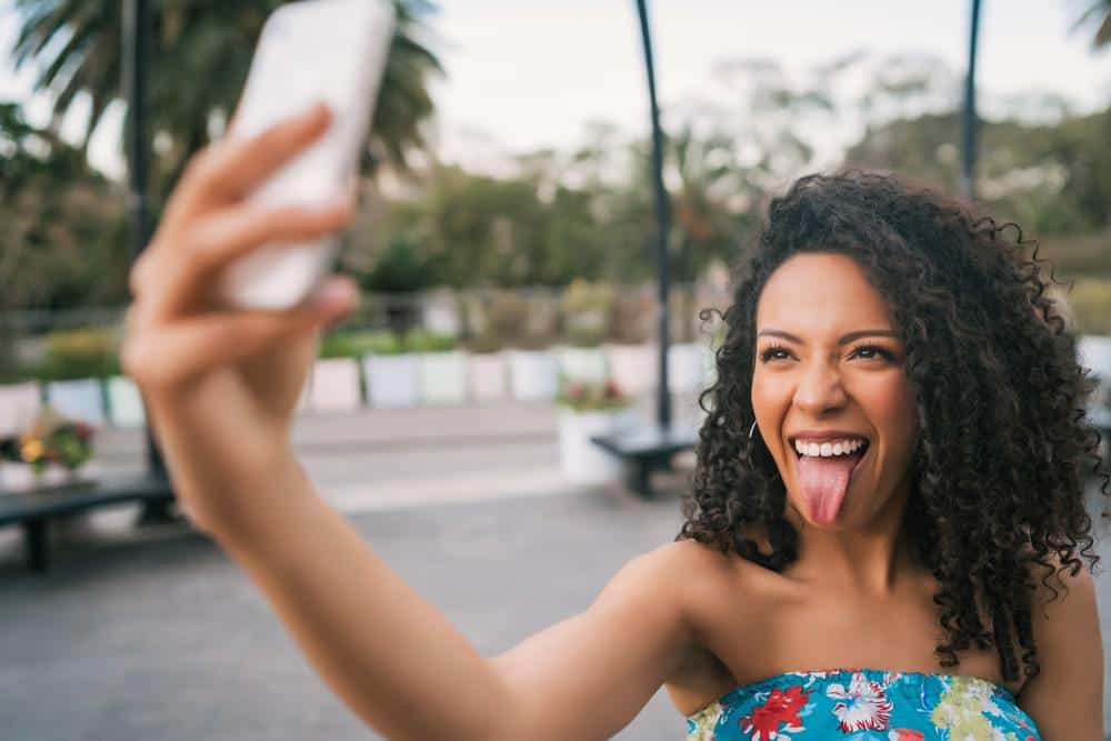 Young African American Latin woman taking a selfie with mobile phone outdoors in the street.