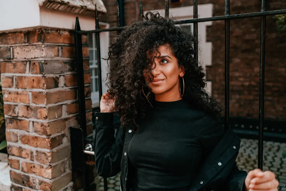 Charming young mixed race female with beautiful curly hair standing outside in front of a black gate looking upward towards the sky.