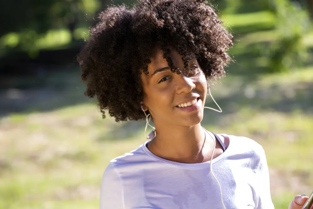 Ylang ylang oil for scalp. Close up portrait of an attractive African Brazilian woman smiling outdoors.