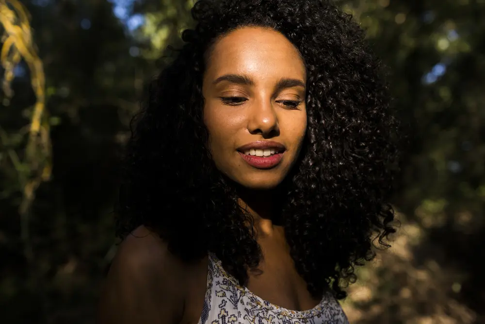 Dark outdoor photo of a beautiful young American woman with wavy hair standing in the woods just before sunset.