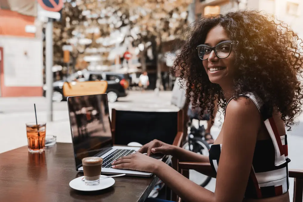 Brazilian businesswoman with very curly type 3a hair using a Macbook Pro while drinking coffee.