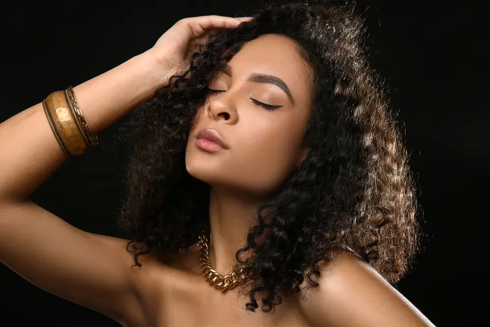 A young black girl with oily hair used a certified-organic hair mask to create a protective skin barrier on her scalp.