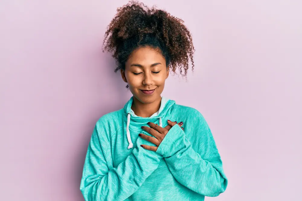 Beautiful African American woman wearing a blue hoodie sweatshirt with her hand over her heart. 