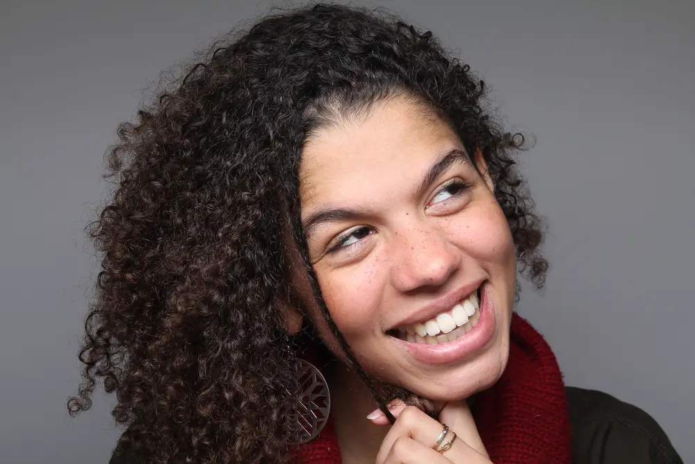 Cute black girl admiring her hair and scalp that's been treated with safflower oil wearing a red scarf, black shirt and silver ring on her finger.