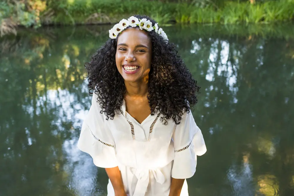 Outdoor photo of a cute young black woman standing in front of the water with type 3b curly hair. 