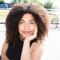 Beautiful mixed-race lady with curly hair sitting on a bench in the center of the city after her hair has been treated with peppermint oil.