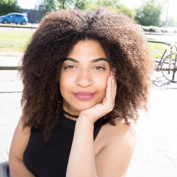 Beautiful mixed-race lady with curly hair sitting on a bench in the center of the city after her hair has been treated with peppermint oil.