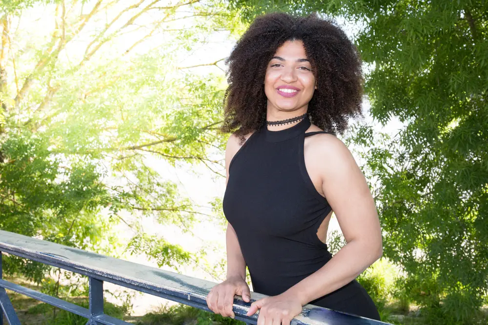 Curly brown girl on a bridge with nice green brushes and trees in the background. 