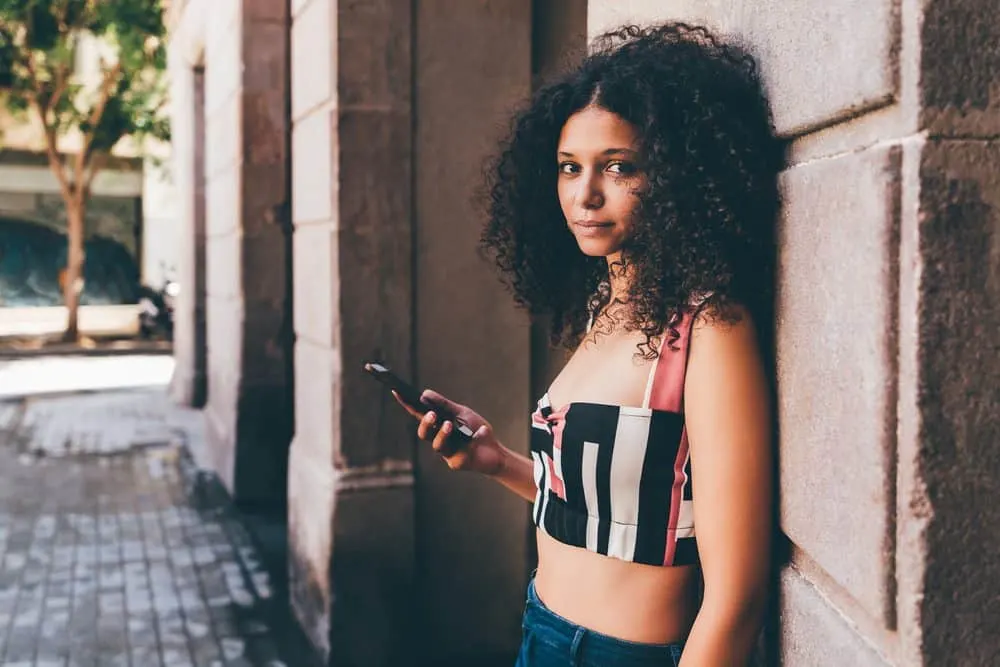 Beautiful Moroccan female with type 2c hair leaning on a brick wall outside.