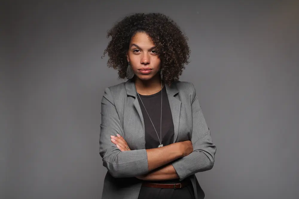 African American female with curly type 3b hair treated with safflower oil wearing a gray jacket and black shirt.