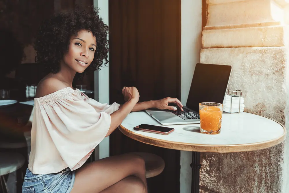 Cute African American woman with perm rods taking a picture with her iPhone while sitting at an outdoor bar on a bright autumn day.