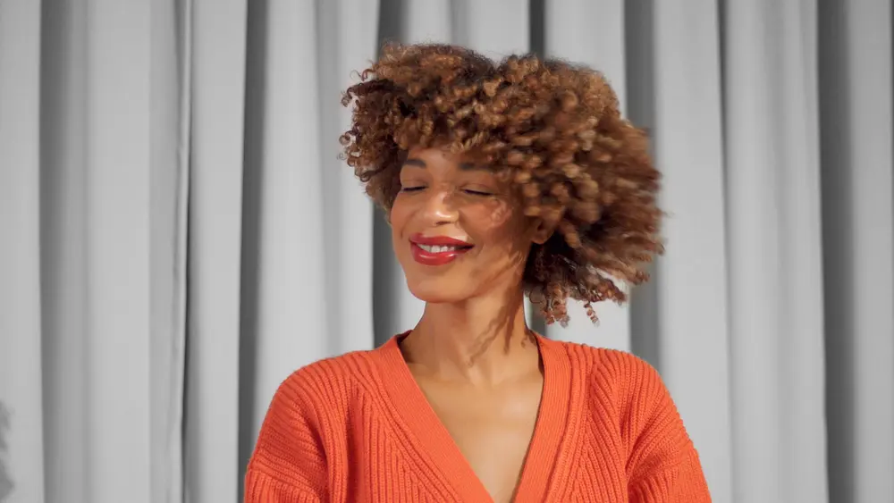 Beautiful closeup portrait of mixed race black woman smiling and shake her type 3a naturally curly hair while smiling.