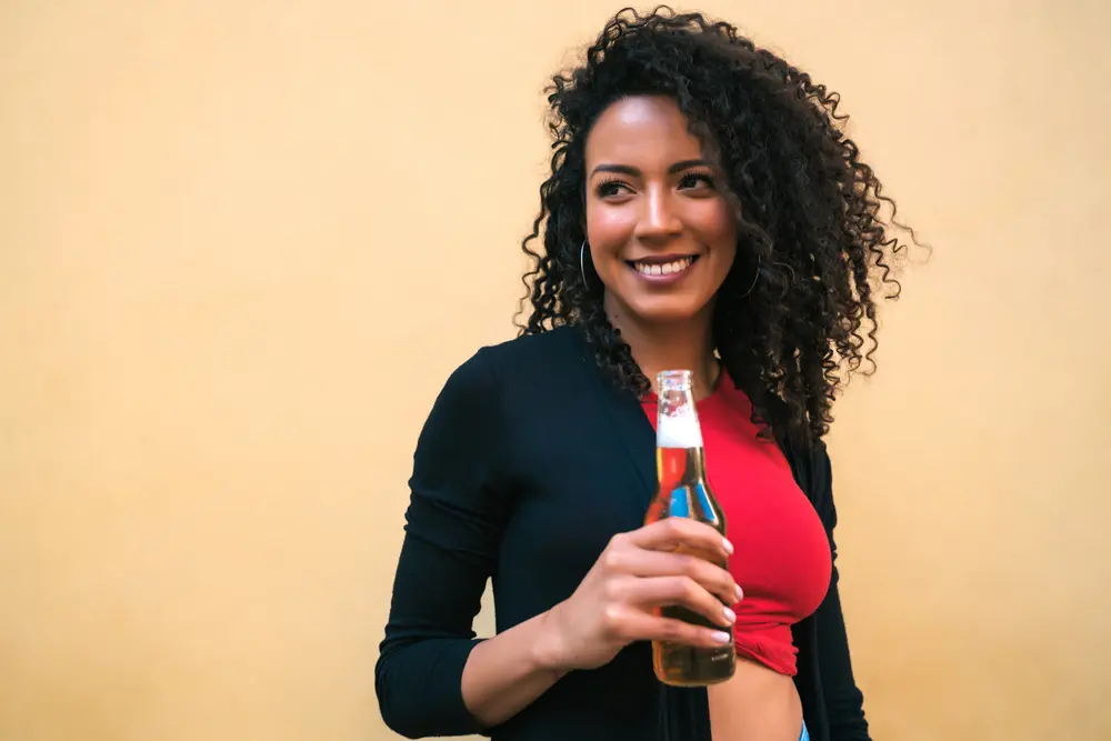 Young American Latin woman with carrier oil treated curly hair enjoying and drinking a bottle of coke.