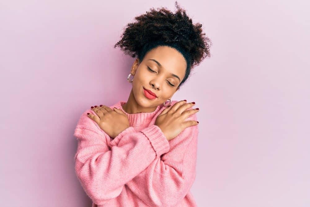 Young African American girl wearing a pink sweater hugging herself with red lipstick. 