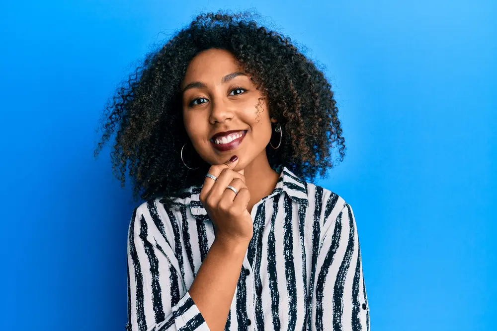 Beautiful African American woman with afro hair wearing casual clothes smiling looking confident at the camera with crossed arms and hand on chin.