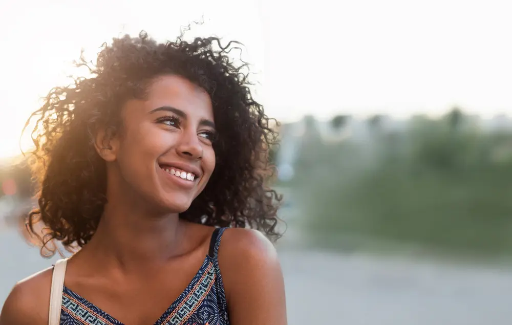 Beautiful black woman with naturally curly hair on a blurry background while smiling.