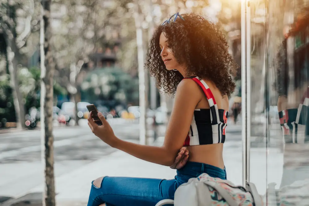 African American women sitting outside on city bench with naturally curly hair after using arnica oil.