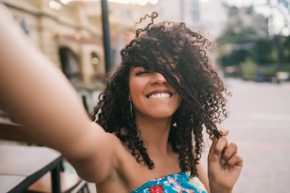 Portrait of a young Afro-American woman with healthy hair taking a selfie outdoors in the street.