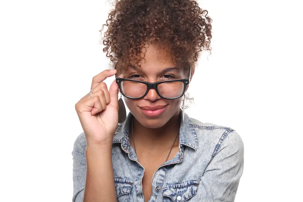 American female wearing black glasses with safflower oil treated curly hair looking directly into the camera while smiling. 