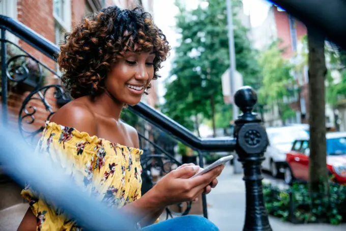 Black girl with 4b curls sitting onside while using her Apple iPhone