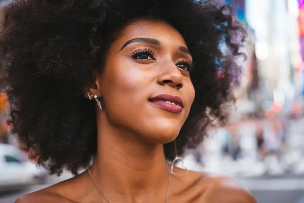 African American woman with a curly girl, healthy hair routine, and arched eyebrows wearing a silver necklace.