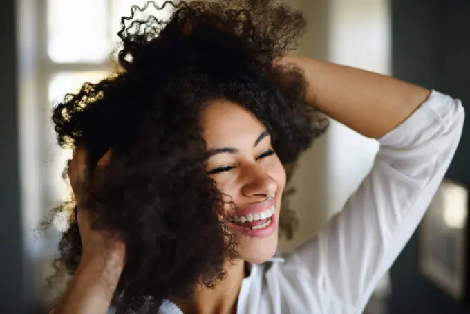 Black lady with a big smile playing in her curly hair strands