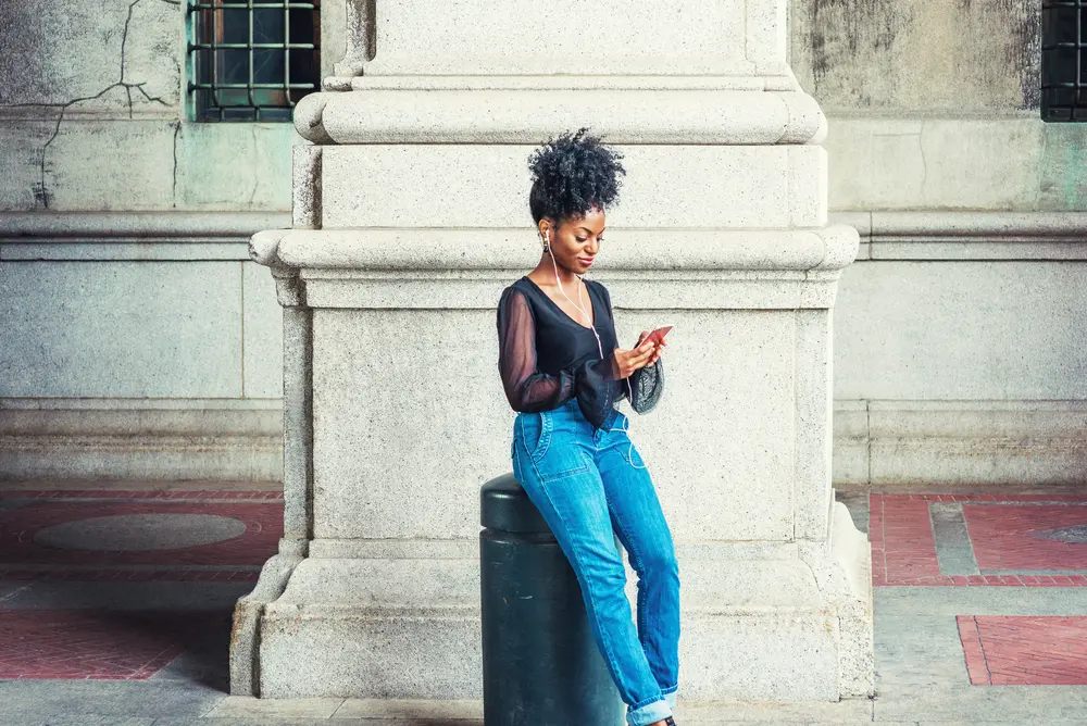 Female with naturally curly hair treated with black seed oil wearing a black shirt and blue jeans.