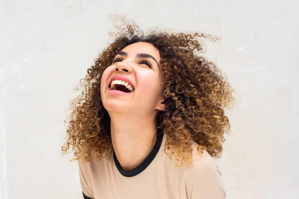 Women with naturally curly hair with a huge smile wearing a badge t-shirt. 