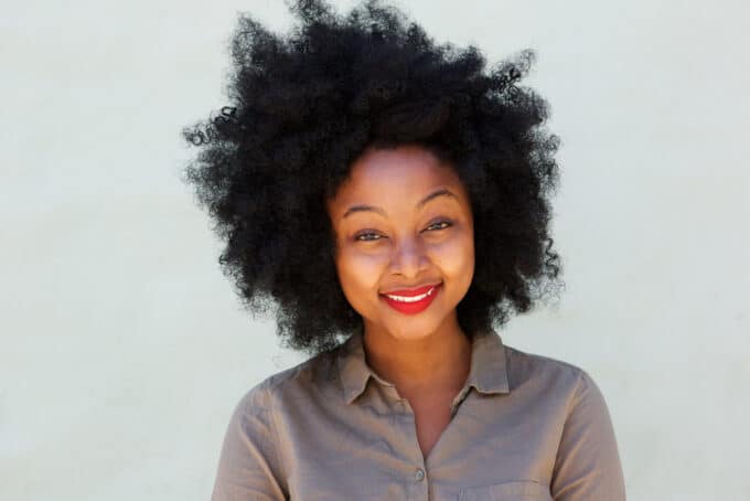 Black woman with curly hair wearing red lipstick and gray collared dress shirt. 