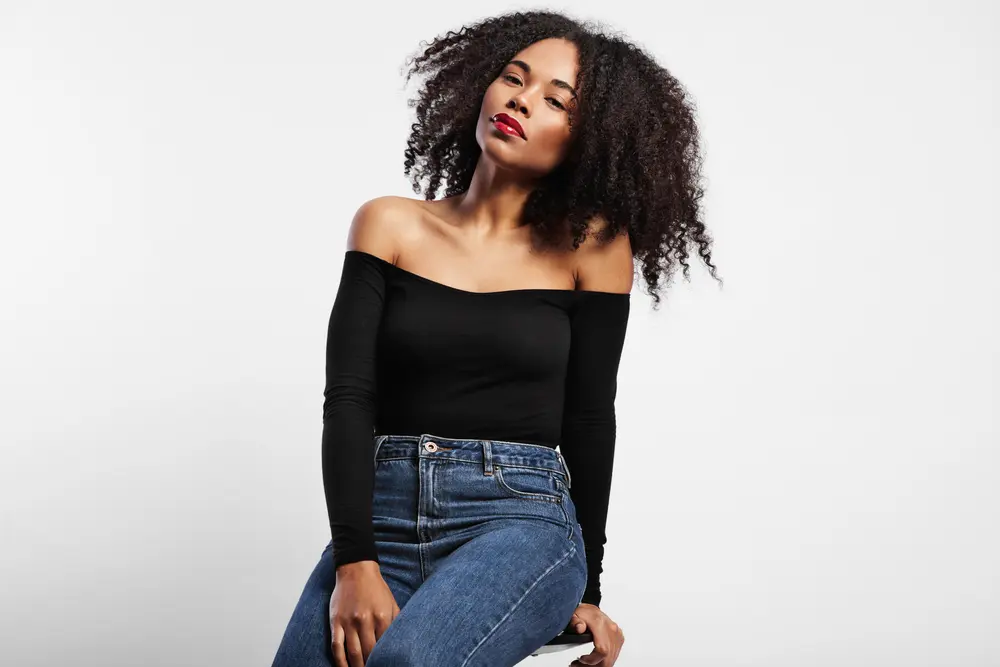 Black adult women sitting on a start wearing blue jeans, and a black shirt, with wavy type 4a natural hair.