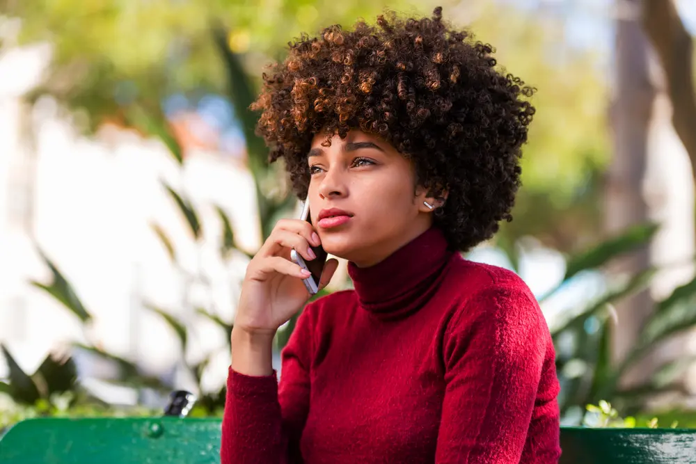 Young African American woman ordering the best moisturizers for low porosity from Amazon while speaking on a mobile phone.