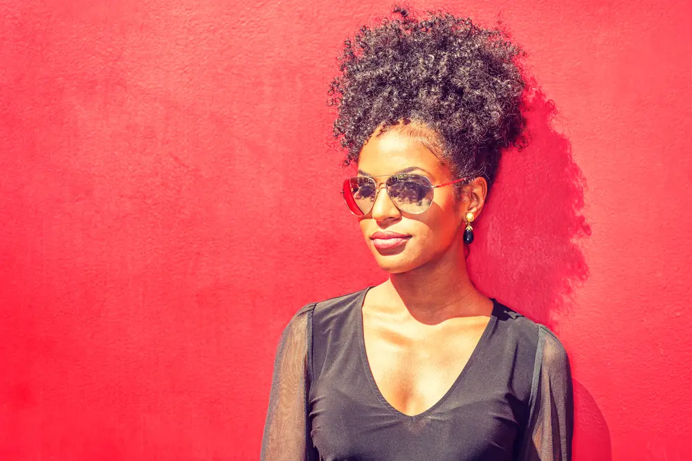 Black women wearing black sheer top in sun with black seed oil treated curly hair. 