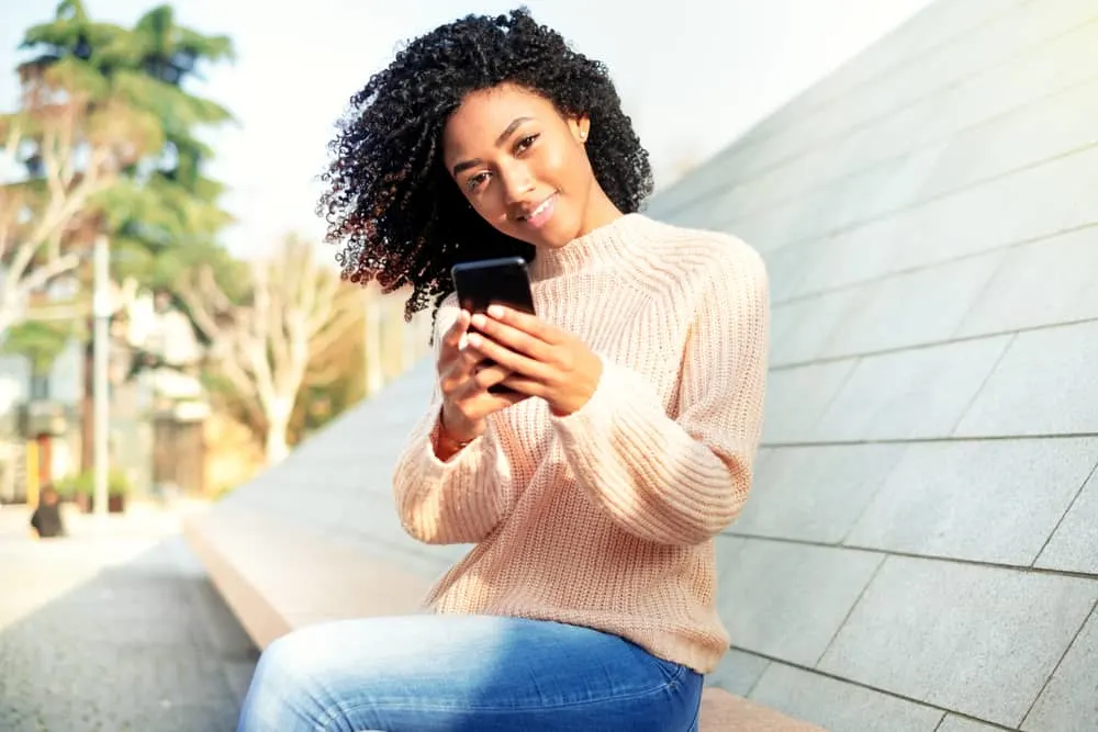 Adult female with a finger coil hairdo watching video tutorials on creating natural curls.