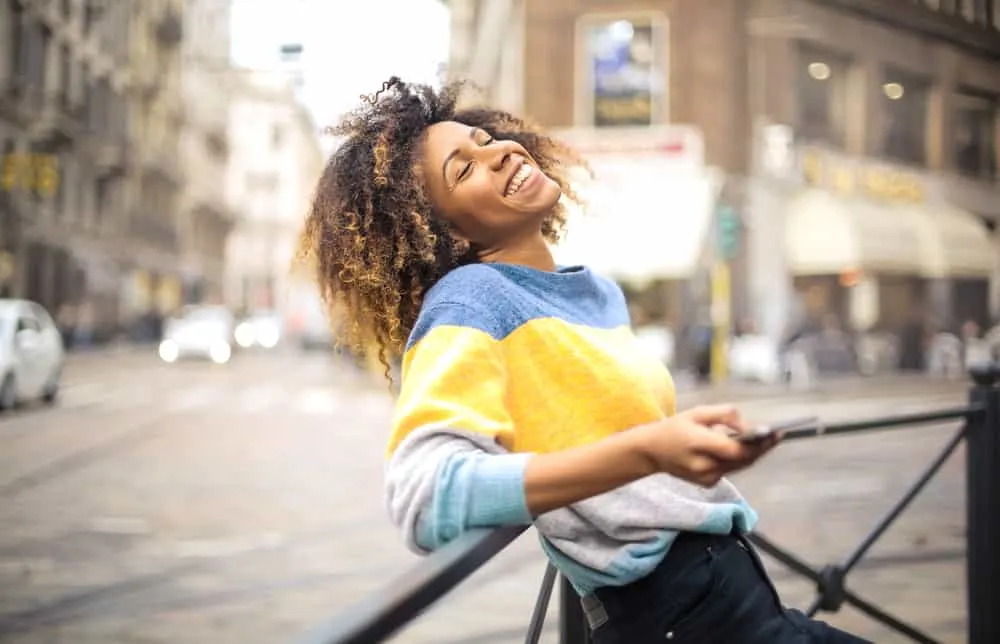 Black women with ombre 4c strands wearing a blue, yellow, and gray sweater with black jeans. 