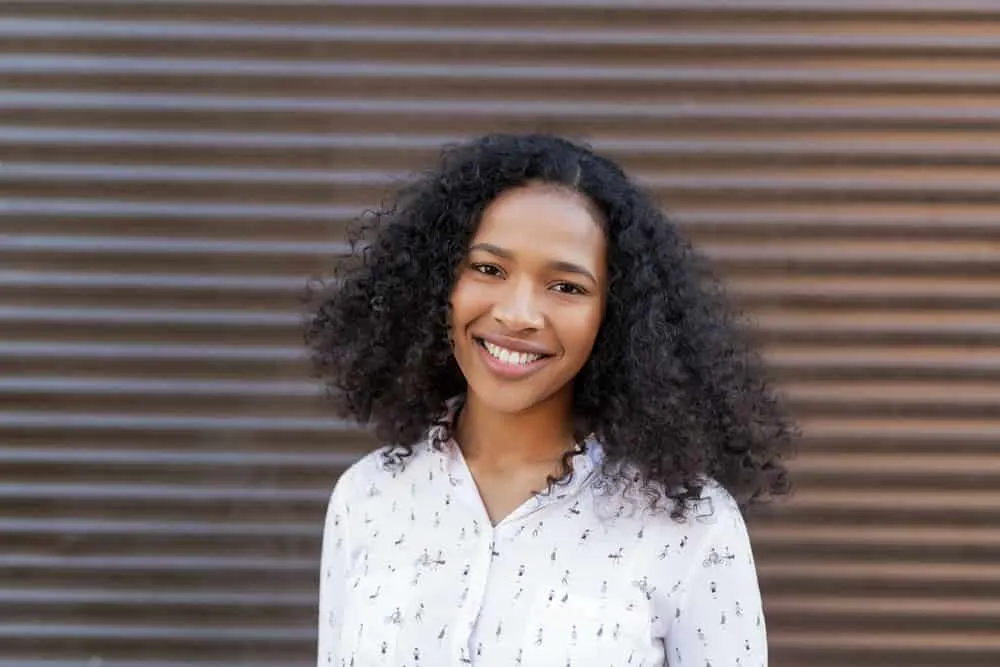 Black women leaning on a wooden barrier while smiling at the camera and holding the side of her face. 