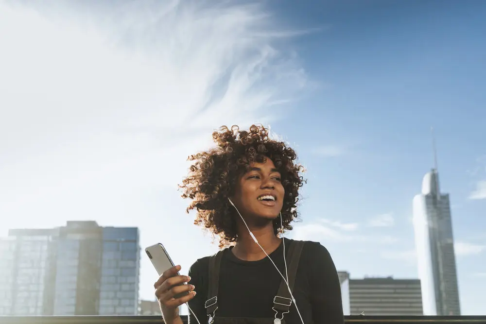 American female with type 3 curly hair using an iPhone 10 outdoors. 