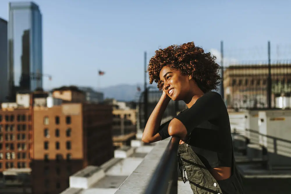 Black women with naturally curly hair wearing green overalls standing on a building rooftop in Los Angeles, CA.