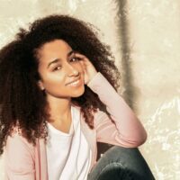 Beautiful African American female sitting on the ground near a grunge wall.