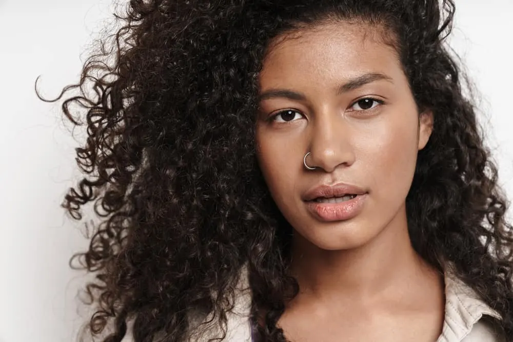 Young black woman looking directly into the camera with a nose ring and type 3b curly hair strands. 