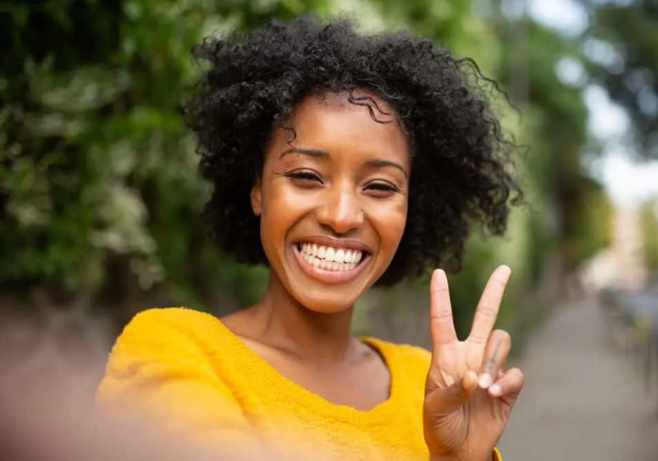 Black female holding up the peace sign with her fingers while taking a selfie with her mobile phone.