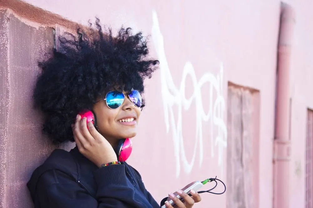 Black girl with natural hair listening to the song Next Day by the Cold Water band on her headphones.