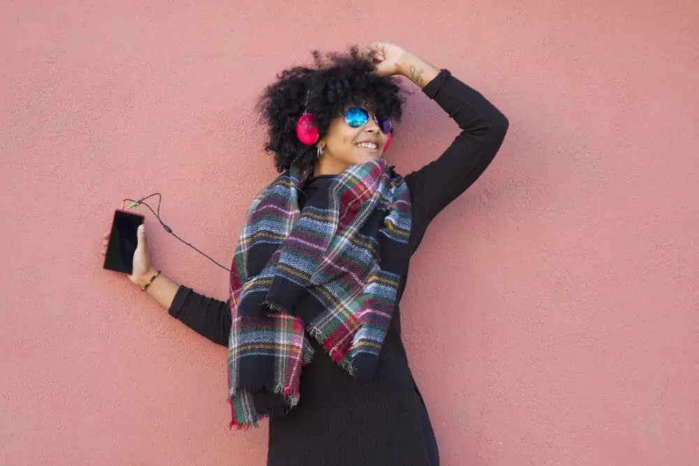 Black women dancing in the street while wearing a black dress, headphones, and a multi-colored winter scarf. 