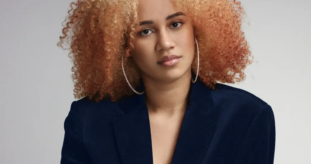 Cute mixed-race lady with curly afro and diamond hoop earrings wearing a blue business suit